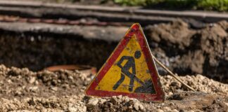 “공사 중, 참아 주셔서 감사합니다.” a dirty roadworks sign standing on a pile of dirt